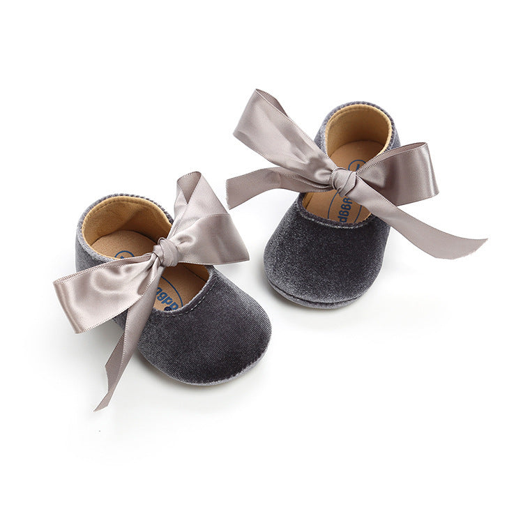 Soft gray baby shoes with delicate ribbon ties and a flexible sole, perfect for toddlers' first steps. Discover more at beekaaboo.com