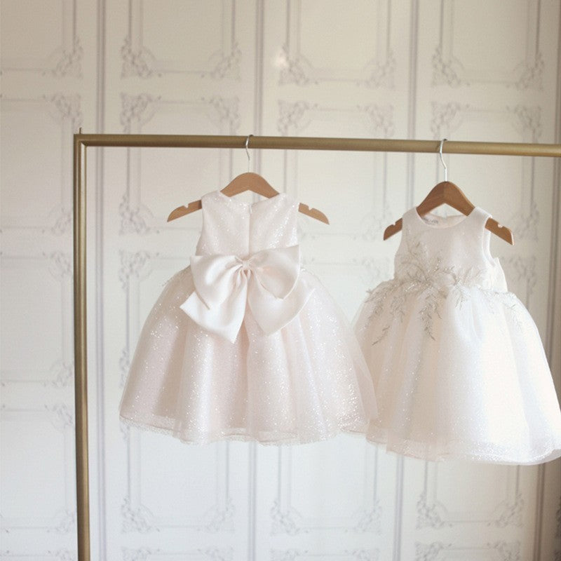 Display of two white sleeveless princess dresses with back bows, hanging on wooden hangers – elegant and formal girls’ wear – beekaaboo.com