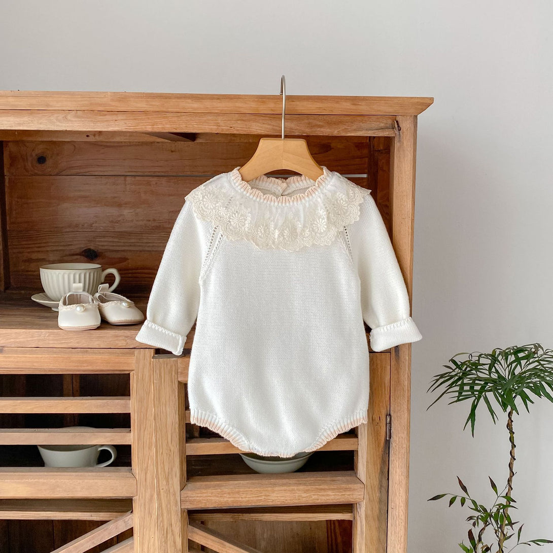 White baby dress with lace details on a wooden hanger against a wooden cabinet | beekaaboo.com