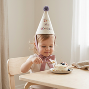 Baby wearing soft birthday party hat with pom detail while eating cake beekaaboo.com