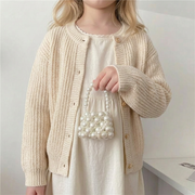 Swedish girl wearing soft Scandinavian kidswear holding a mini pearl handbag in a neutral boutique setting – beekaaboo.com