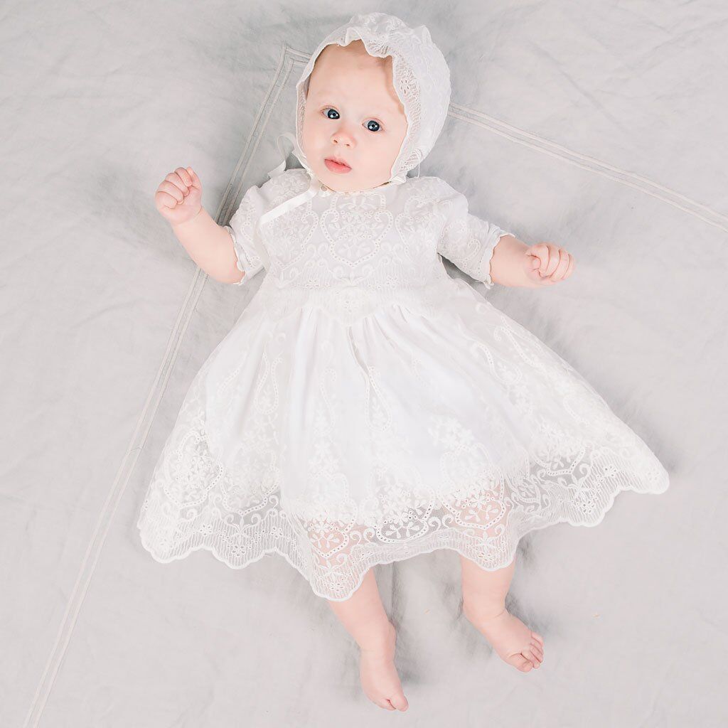 Baby wearing long sleeve baptism dress and bonnet, seated and smiling – beekaaboo.com